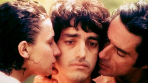 Trois visages en gros plan : un homme se faisant embrasser sur chaque joue par un autre homme et une femme